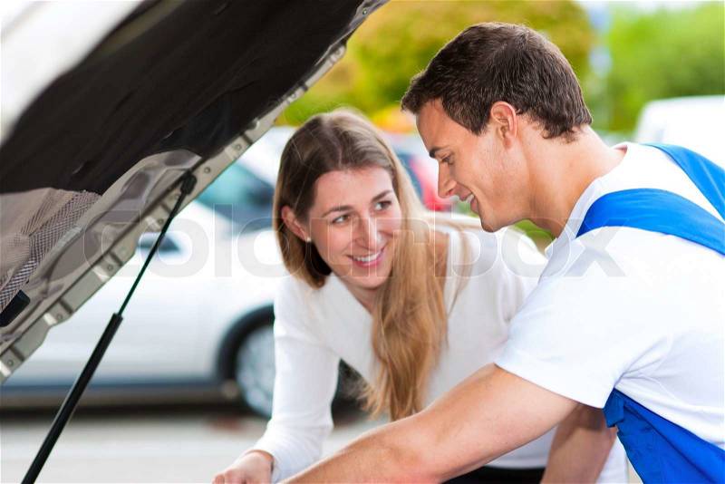 Woman talking to a car mechanic in a parking area, both are standing next to the car, stock photo