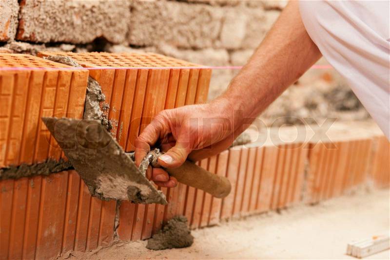 Bricklayer laying, well, bricks to make a wall, he is pulling grout out of a joint with his trowel. This man is really working hard, stock photo
