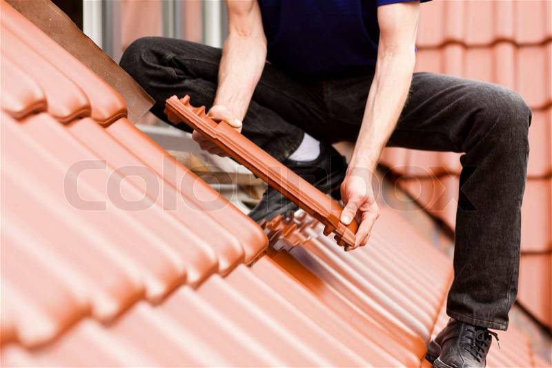 Roofing - construction worker standing on a roof covering it with tiles, stock photo