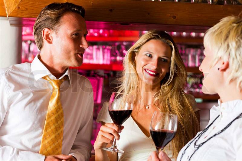 Man and two women in a hotel bar in the evening having glasses of red wine and probably a little flirt, stock photo