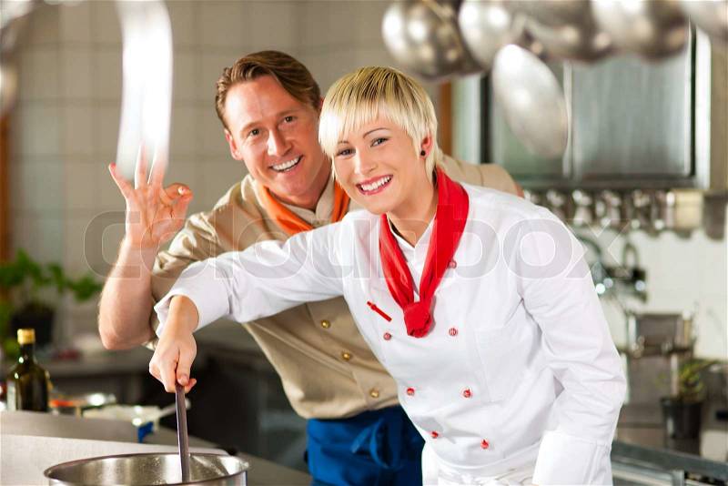 Two chefs in teamwork - man and woman - in a restaurant or hotel kitchen cooking delicious food, stock photo