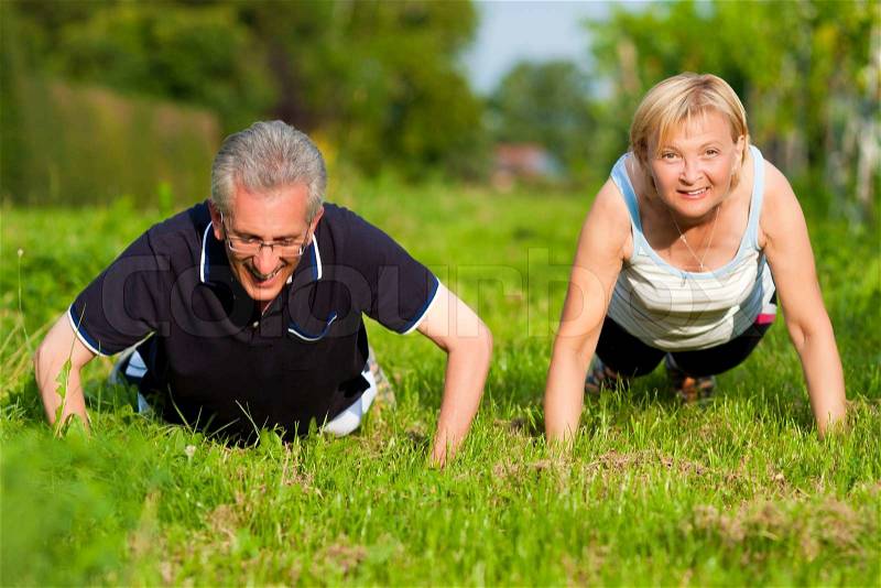 Mature or senior couple in jogging gear doing sport and physical exercise outdoors, pushups, stock photo
