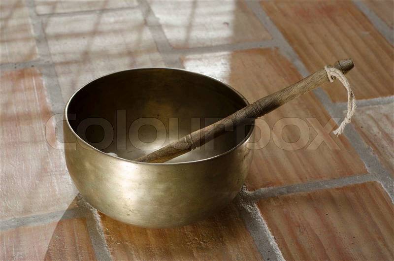 A Tibetan singing bowl sitting on a tiled floor with a baton resting inside, stock photo