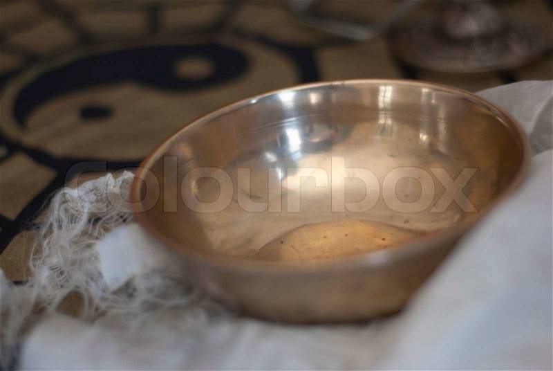 A gleaming brass Tibetan singing bowl, on a white buddhist scarf with soft focusedblack and gold ying yang, stock photo