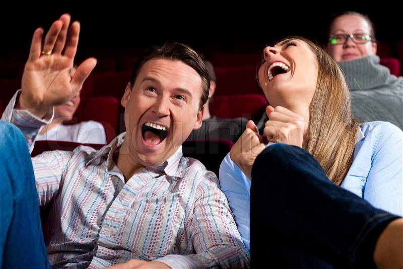 Couple and other people, probably friends, in cinema watching a movie, it seems to be a funny movie, stock photo