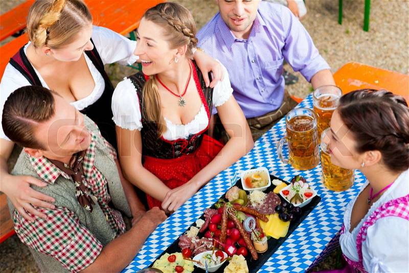 In Beer garden - friends Tracht, Dirndl and on a table with beer and snacks in Bavaria, Germany, stock photo