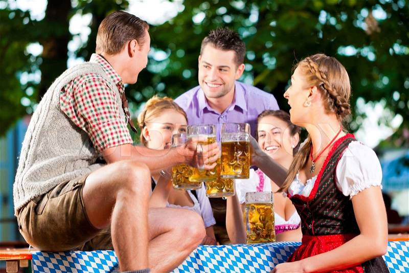 In Beer garden - friends in Lederhosen drinking a fresh beer in Bavaria, Germany, stock photo