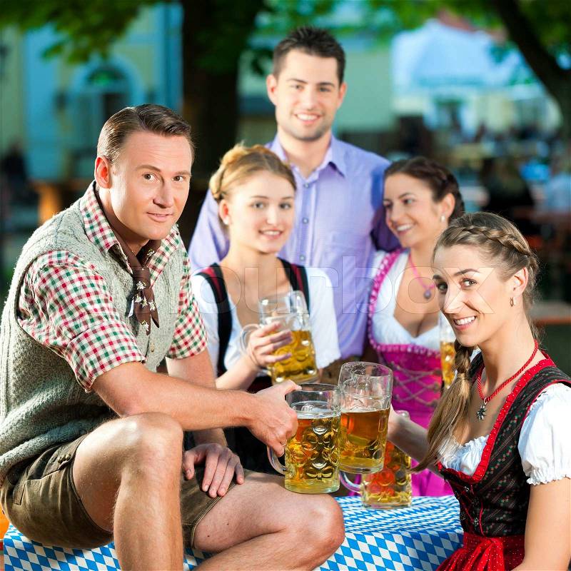 In Beer garden - friends in Lederhosen drinking a fresh beer in Bavaria, Germany, stock photo