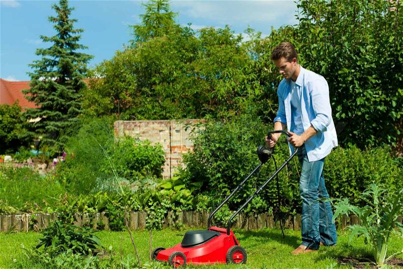 Young man is mowing the lawn in summer with a mowing machine, stock photo