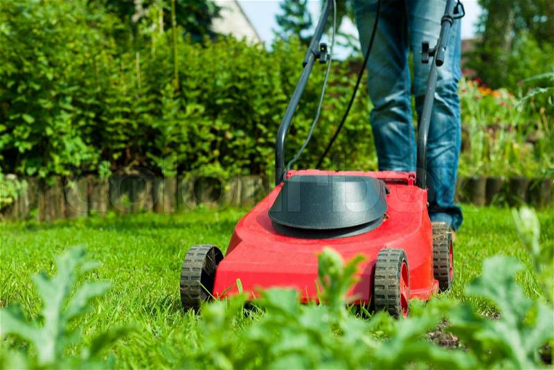 Young man - only legs to be seen - is mowing the lawn in summer with a mowing machine, stock photo