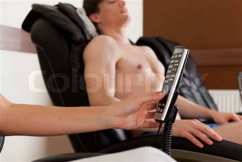 Young couple is recovering on massage chair in gym after exercising for their fitness, the woman is holding the remote control for the chair, stock photo