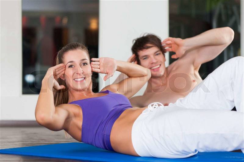 Young couple - man and woman - exercising by doing sit-up, \
