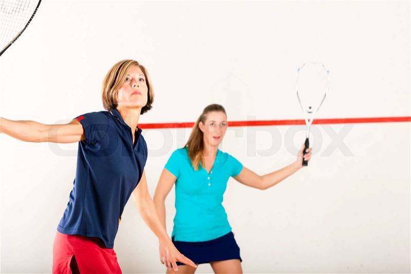 Two women playing squash as racket sport in gym, it might be a competition, stock photo