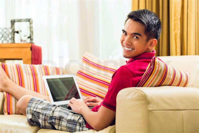 Asian man sitting on couch and surfing the internet and playing game, stock photo