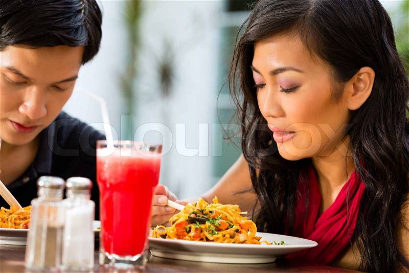 Asian man and woman in restaurant eating their food with chopsticks, stock photo