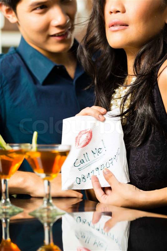 Asian woman seduces the man in restaurant and gives him her number on a napkin, stock photo