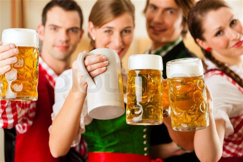 Young people in traditional Bavarian Tracht in restaurant or pub with beer and steins, stock photo