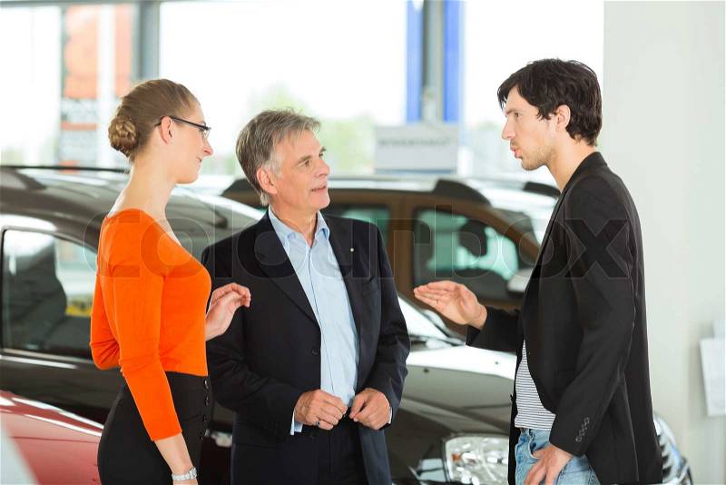 Mature single man with autos in light car dealership with a young couple,- man, young -, he obviously is buying a car or is a car dealer, stock photo