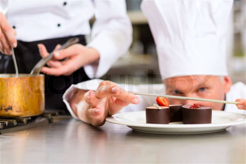 Cook, the pastry chef, in hotel or restaurant kitchen cooking, he is finishing a sweet dessert, stock photo