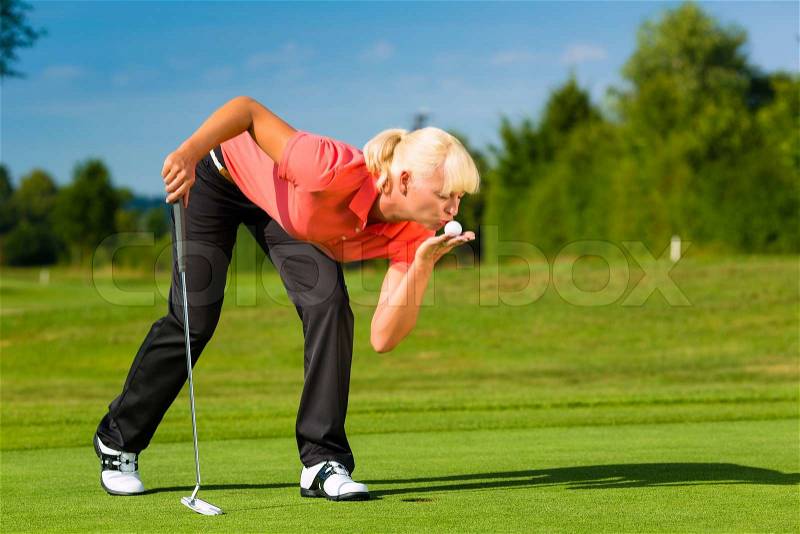 Young sportive couple playing golf on a golf course, she gives the ball a kiss, stock photo