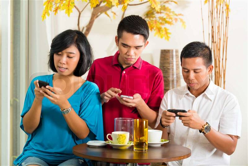Asian people having fun together with mobile phone and drinking coffee or cocktail, stock photo