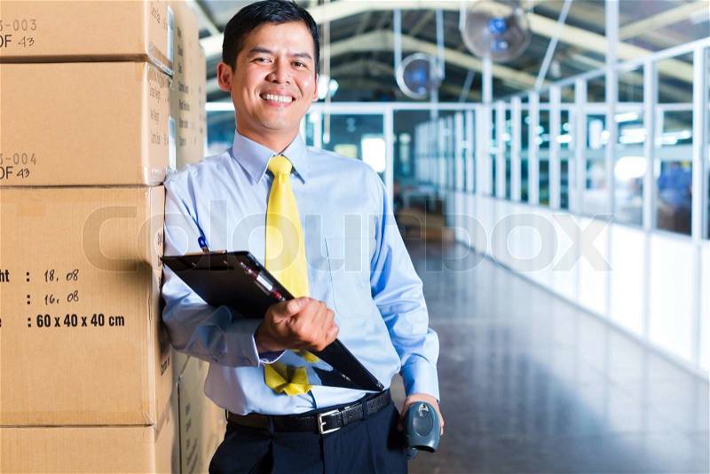 Young Indonesian man in a suit with a bar code scanner in a Asian warehouse of forwarding or logistics company, stock photo