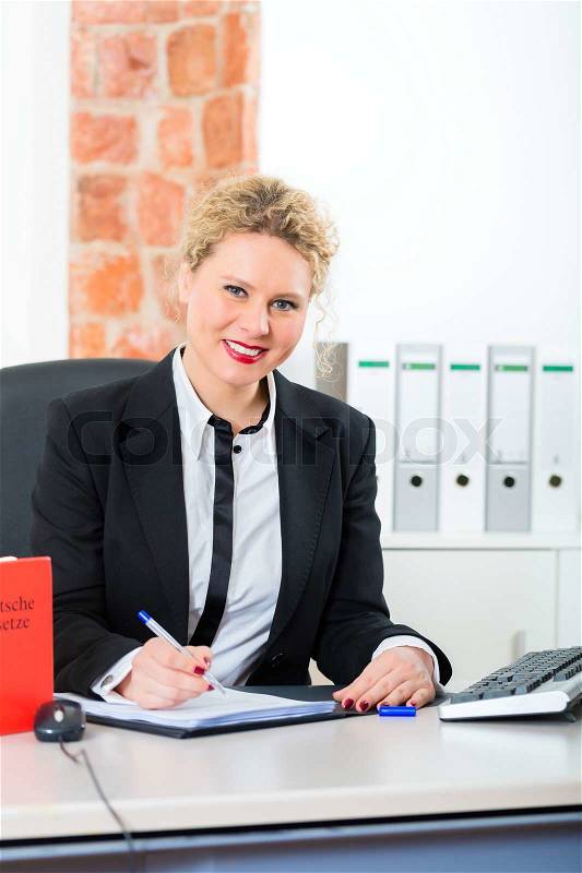 Young female lawyer working in her office with typical law book and writing document, stock photo