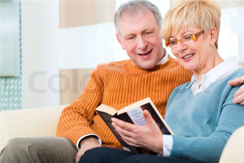 Quality of life - two elderly people sitting at home on the couch, he embraces his wife, stock photo