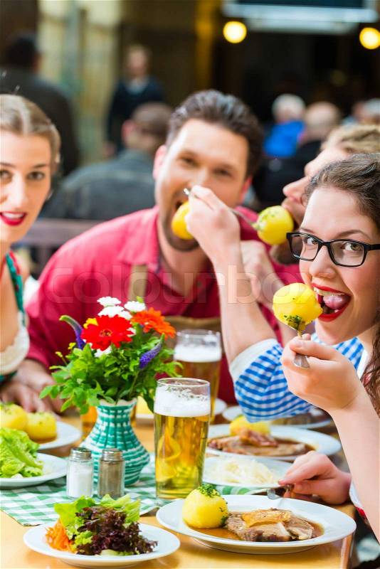 Young people in traditional Bavarian Tracht eating pork in restaurant or pub for lunch or dinner, stock photo