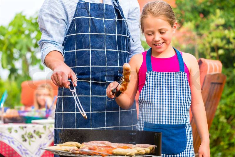 Father and daughter making barbecue in the garden in summer with sausages and meat, stock photo