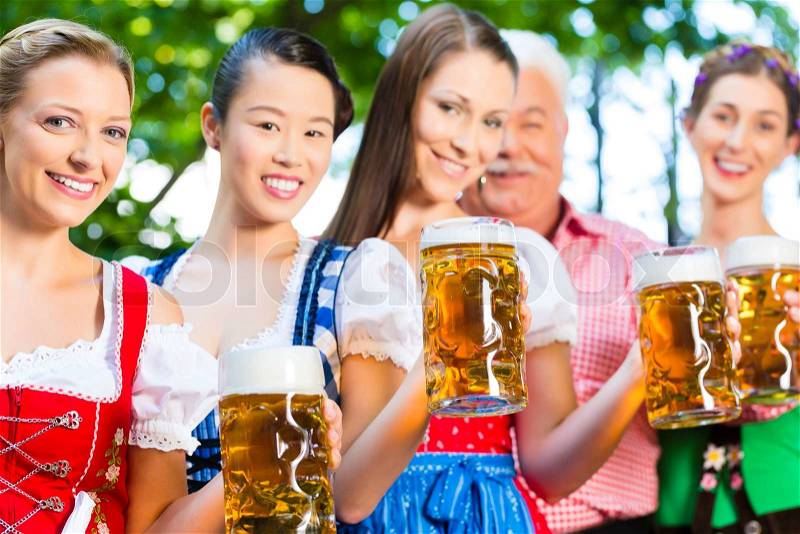 In Beer garden - friends, man and women in Tracht, Dirndl and Lederhosen drinking a fresh beer in Bavaria, Germany, stock photo