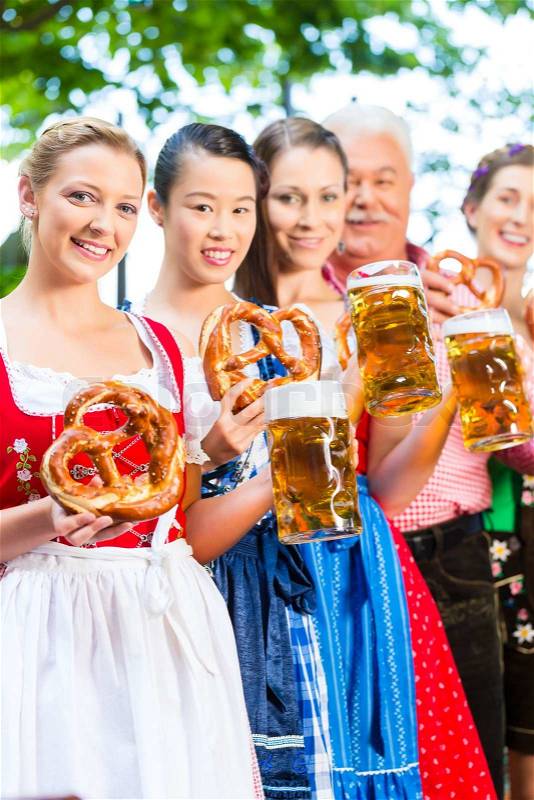 In Beer garden - friends, man and women in Tracht, Dirndl and Lederhosen drinking a fresh beer in Bavaria, Germany, stock photo
