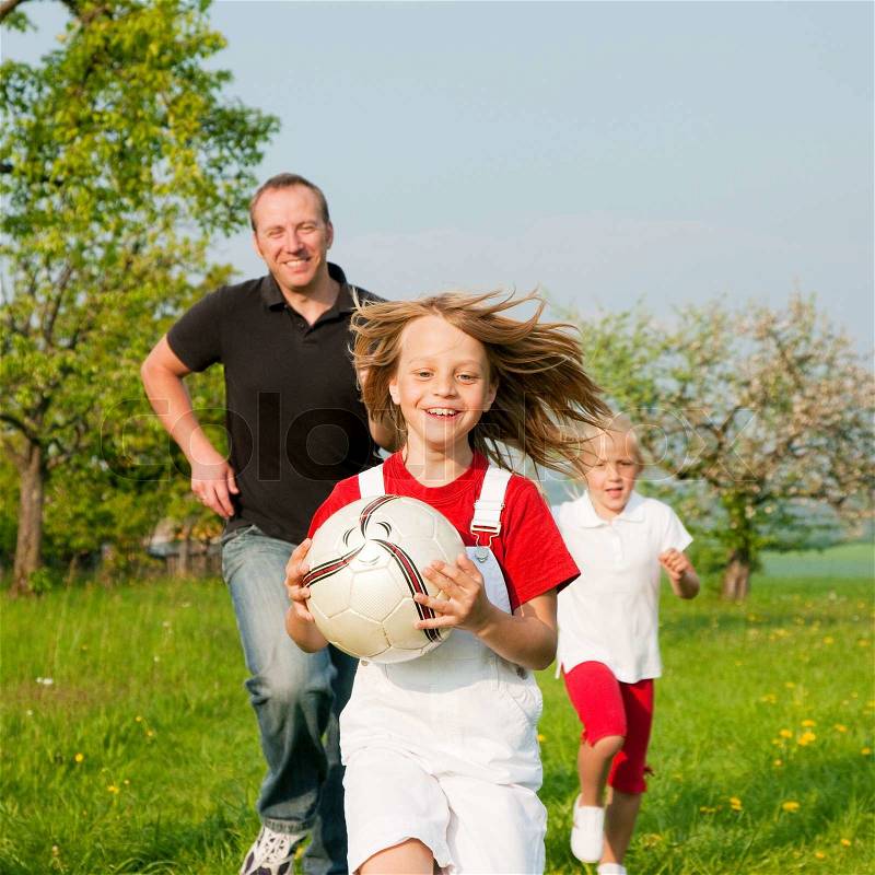 Happy family playing football, one child has grabbed the ball and is being chased by the others, stock photo