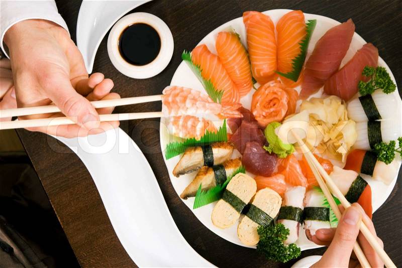 Two people (only hands to be seen) eating sushi; focus on the food, stock photo