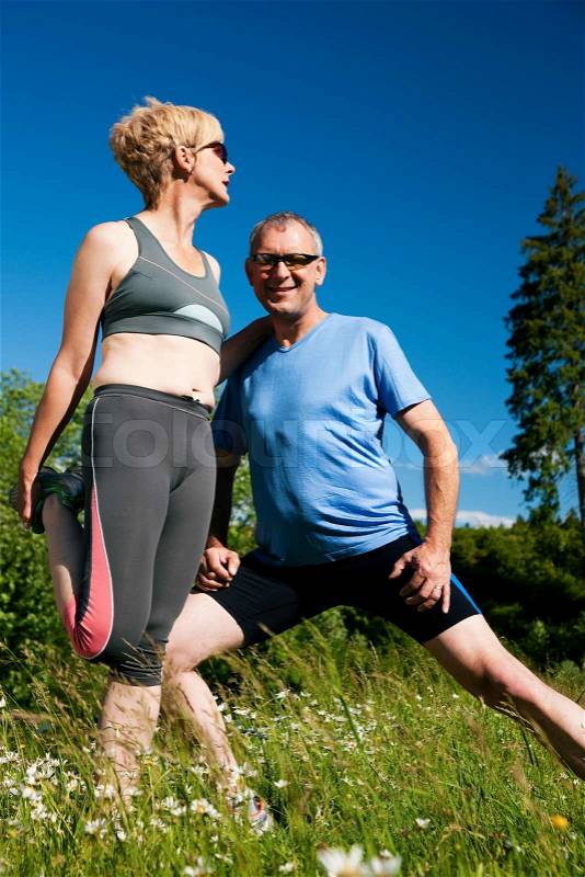 Mature or senior couple in jogging gear doing sport and physical exercise outdoors, stretching and gymnastics, stock photo