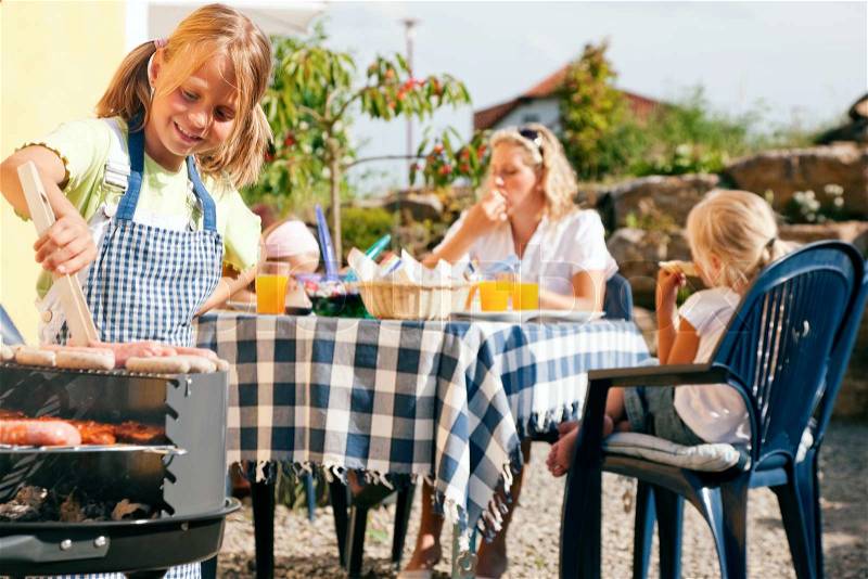 Family having a barbecue party - little kid at the barbecue grill preparing meat and sausages, stock photo