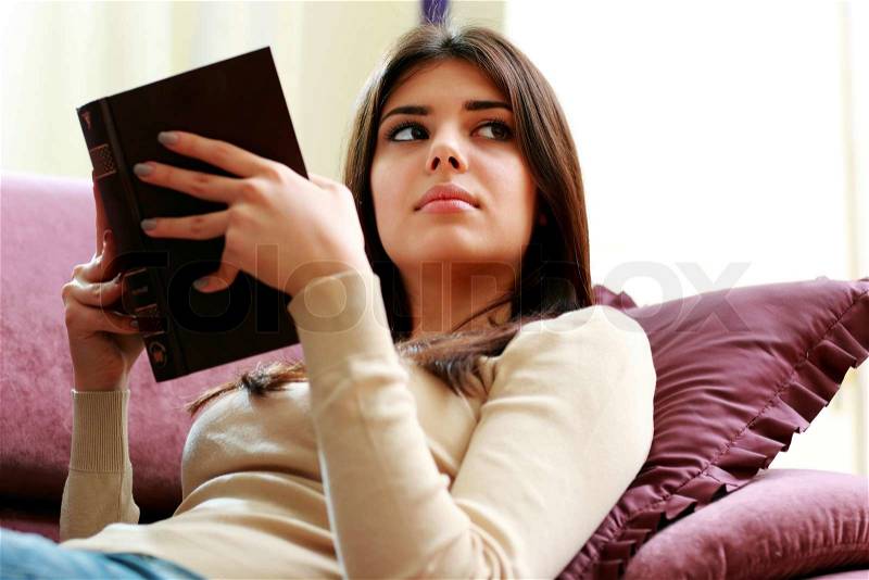 Young beautiful woman holding a book and looking away at home, stock photo