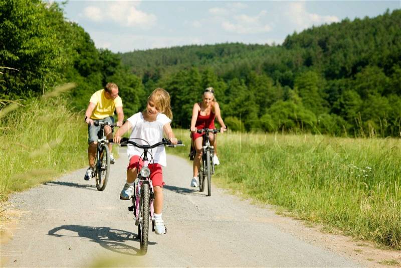 Family with one child riding their bicycles on a summer day (focus on the girl in front), stock photo
