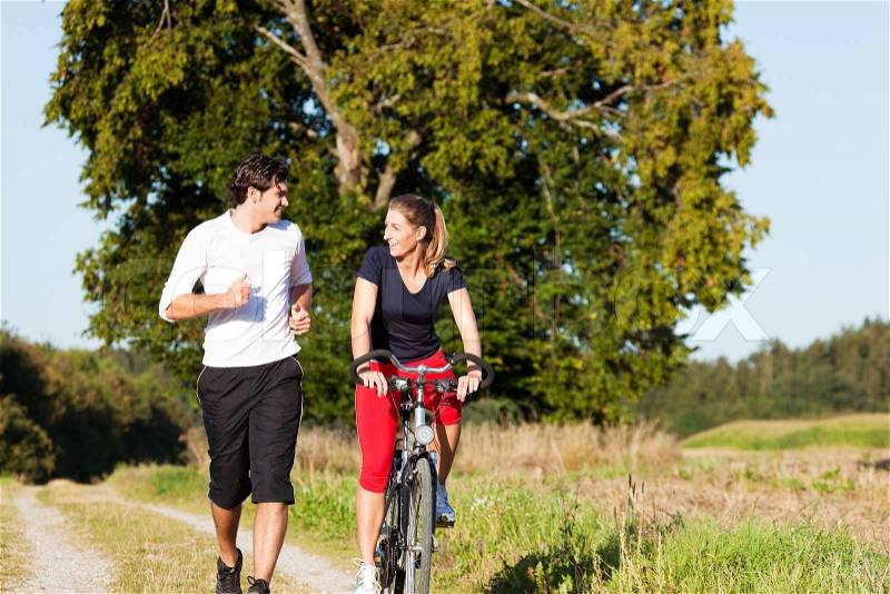 Young fitness couple doing sport outdoors, jogging and riding a bicycle in autumn under a clear blue sky, stock photo