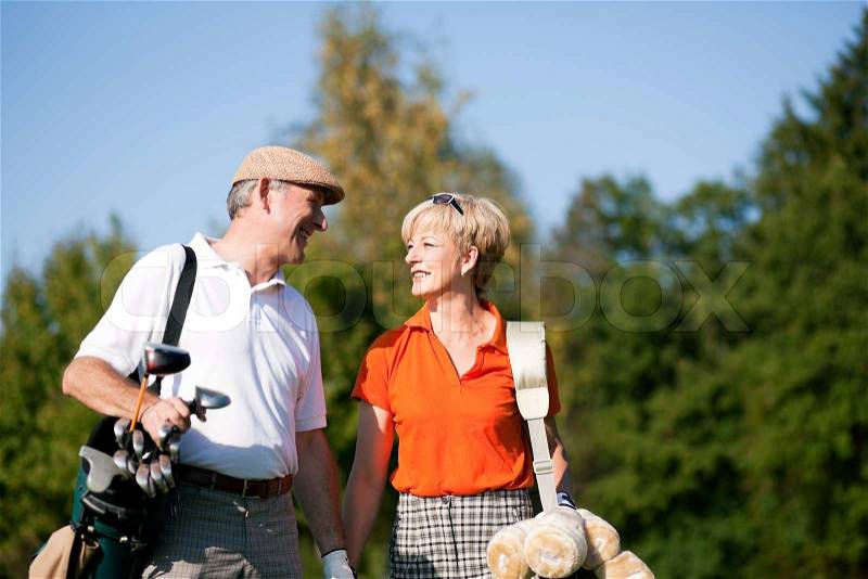 Mature or senior couple playing golf, walking down the course, stock photo