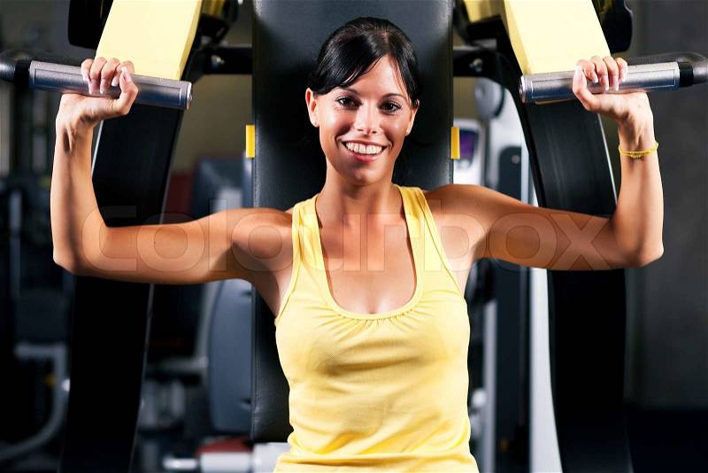 Very fit and beautiful young woman in a gym working out and lifting weights on an exercising machine, stock photo