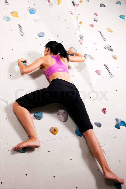 Woman exercising arms and upper body at a climbing wall in a gym, stock photo