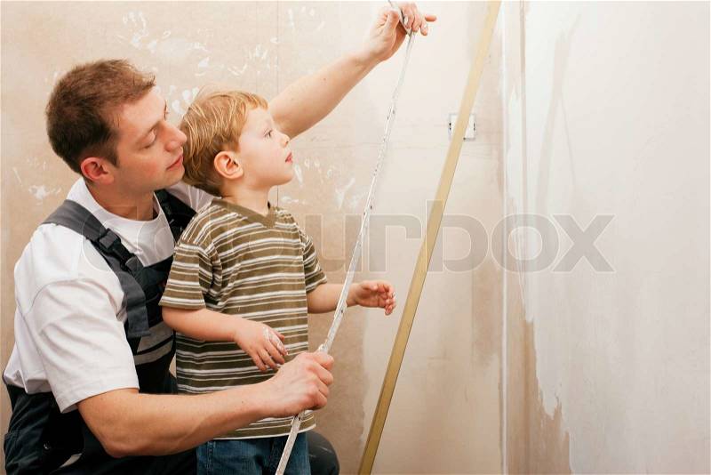 Father and son measuring a dry wall in their home with a folding rule and a bubble level, stock photo
