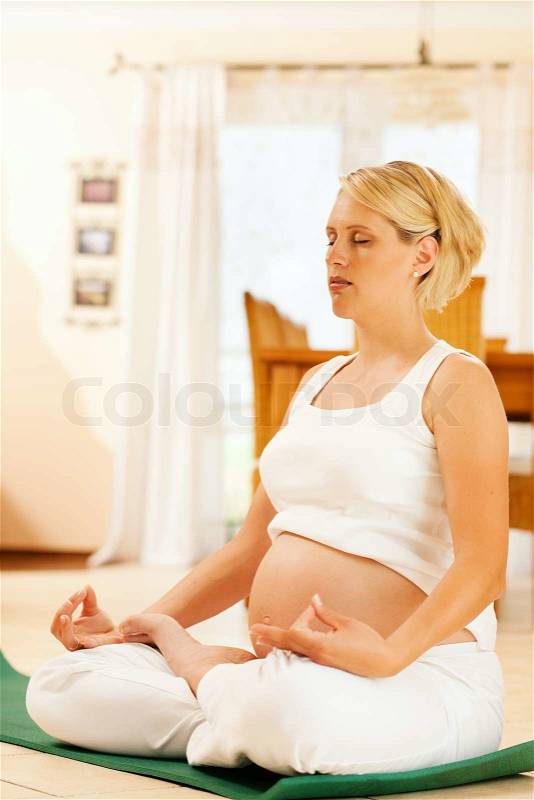 Pregnant woman meditating doing pregnancy yoga sitting on the floor in her home, stock photo