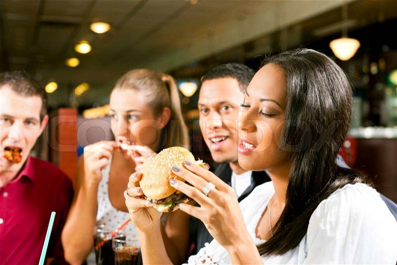 Friends - one couple is African American - eating hamburger and drinking soda in a fast food diner, stock photo
