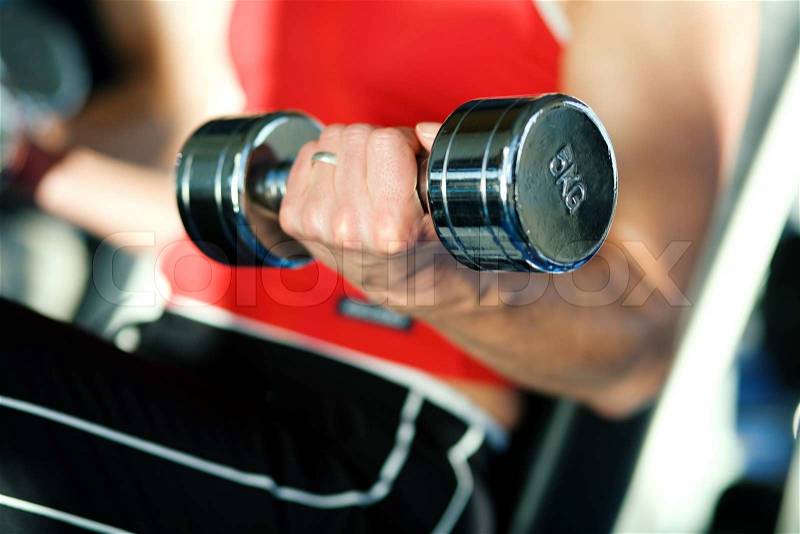 Woman lifting hand weights in a gym, focus on hand of woman and front of dumbbell, stock photo