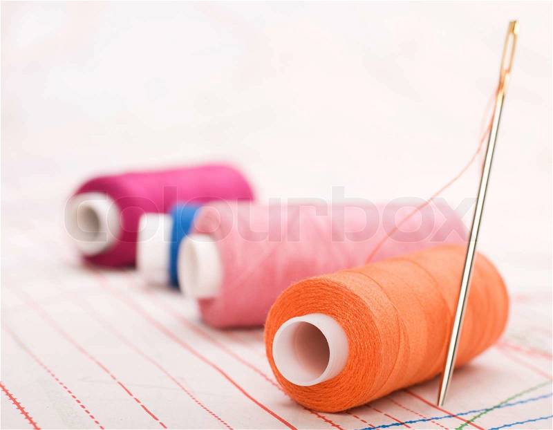 Spool of thread and needle. Sew accessories on blurred background, stock photo