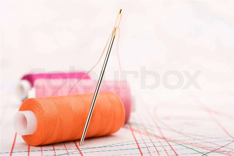 Spool of thread and needle. Sew accessories on blurred background, stock photo