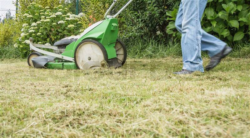 Senior man mowing the lawn with a lawnmower machine, stock photo
