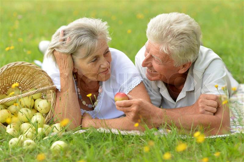 Happy elder couple resting on grass at nature, stock photo